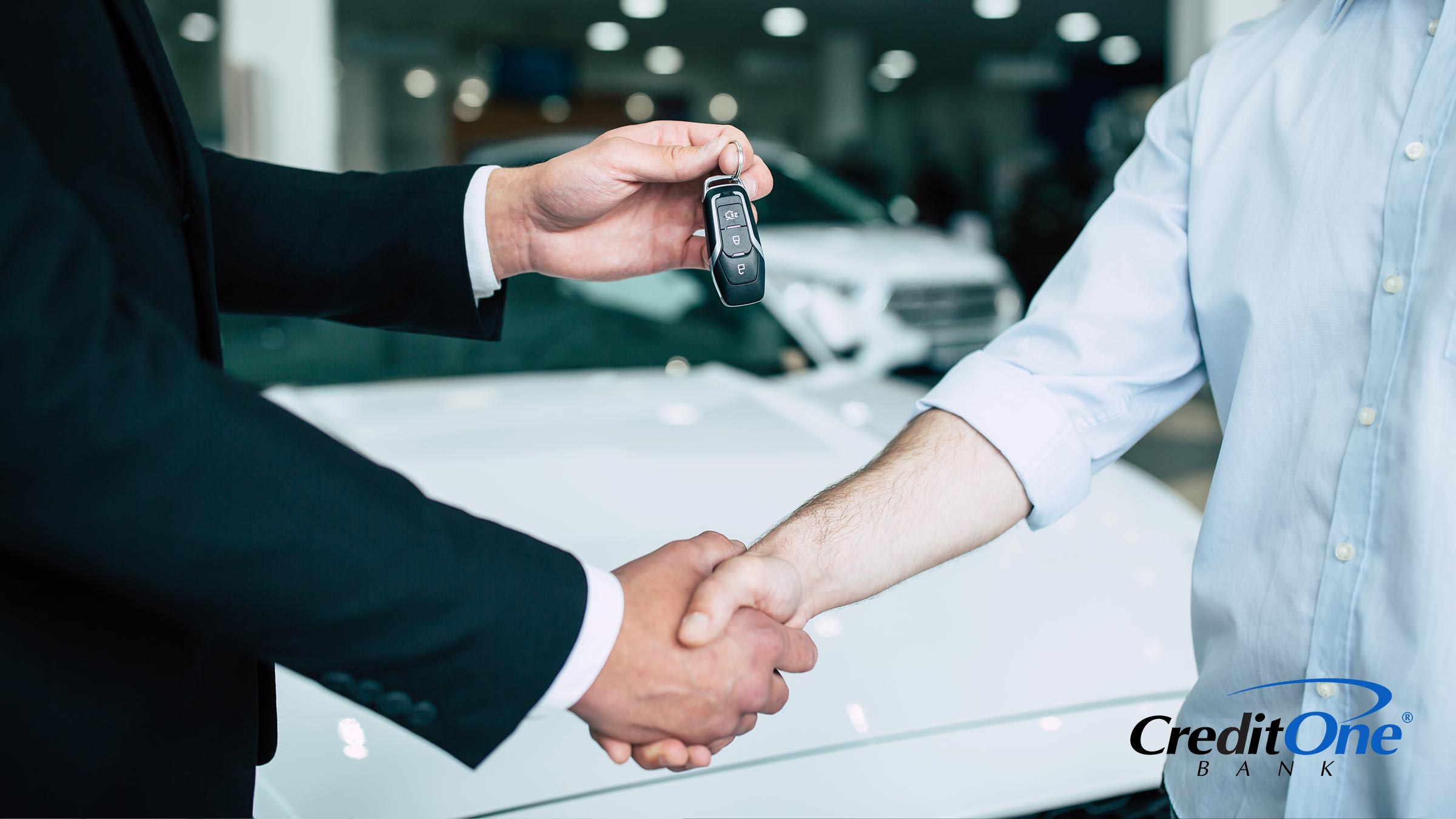 A car dealer hands over the key to a new vehicle while shaking hands with the buyer, who may have purchased the car with a credit card.