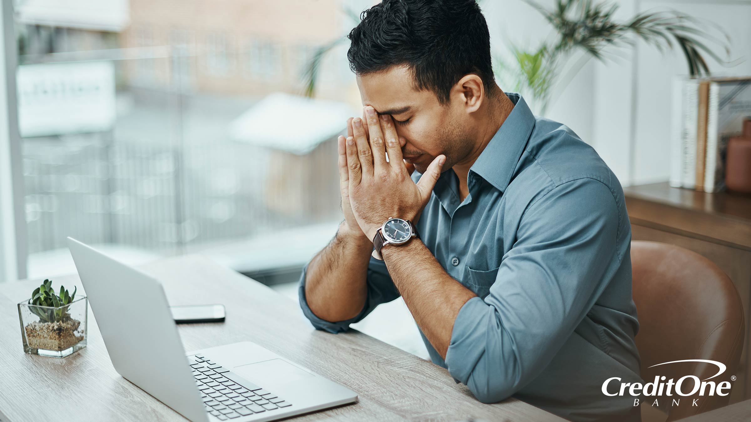 A man sits in front of his laptop with face in hands, looking exasperated as if he might be dealing with a hardship that credit card purchase protection could help with.