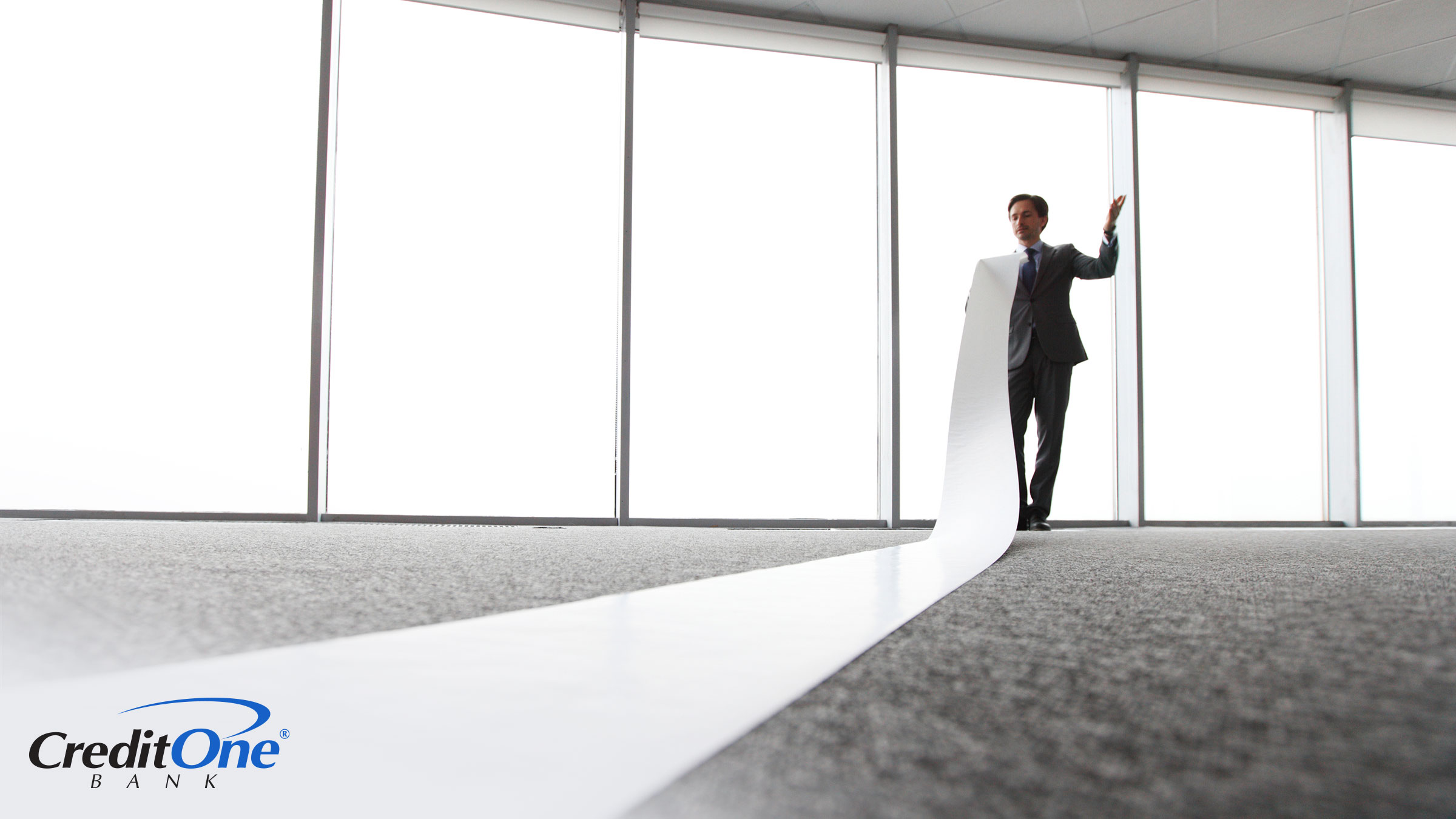 A businessman in an office holds the end of a long and flowing paper report, wondering how the length of his credit history impacts his credit score.