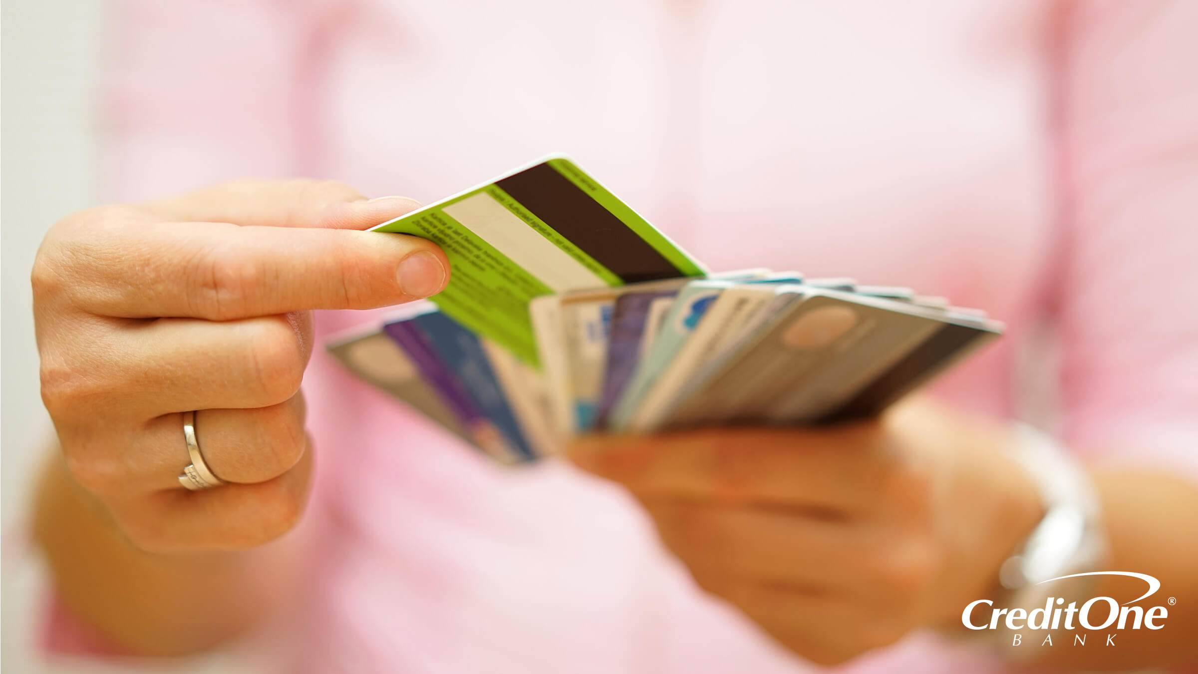 A woman’s hands select one credit card from a fan of many cards, representing the concept that different credit cards may build credit at different rates.