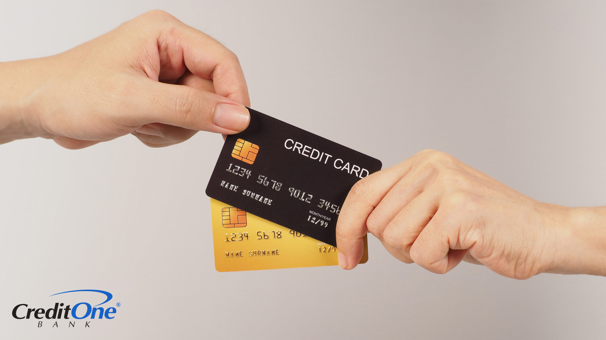 A person’s hand holds two payment cards while another person’s hand selects the credit card from the stack rather than the debit card.