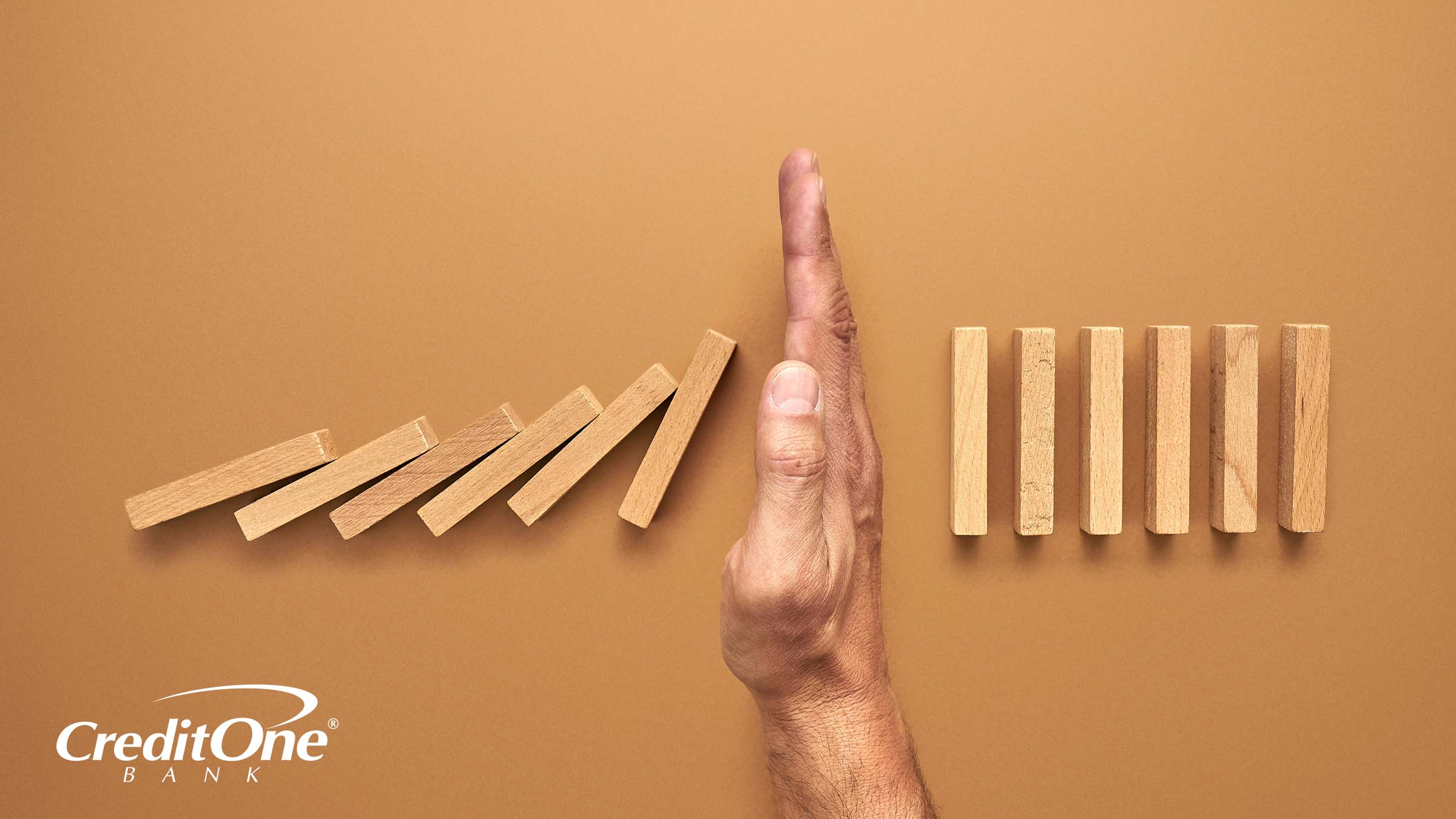 An extending hand reaches out to halt a series of falling dominoes, perhaps signifying how filing for Chapter 7 bankruptcy can halt ongoing debt and provide a fresh start.